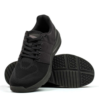 The Women's Ballistic Trainers - Blackout with Black Reflective Spearhead from GORUCK are crafted from breathable mesh and feature black laces and textured rubber soles. One shoe stands upright, highlighting the tread pattern engineered for 3X Stability, making it ideal for fans of functional fitness footwear.