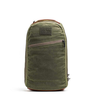 The GORUCK Bullet Ruck - Waxed Canvas in green, with a weathered retro look, stands upright against a plain white background. It includes a front zipper pocket and a subtle patch at the top.