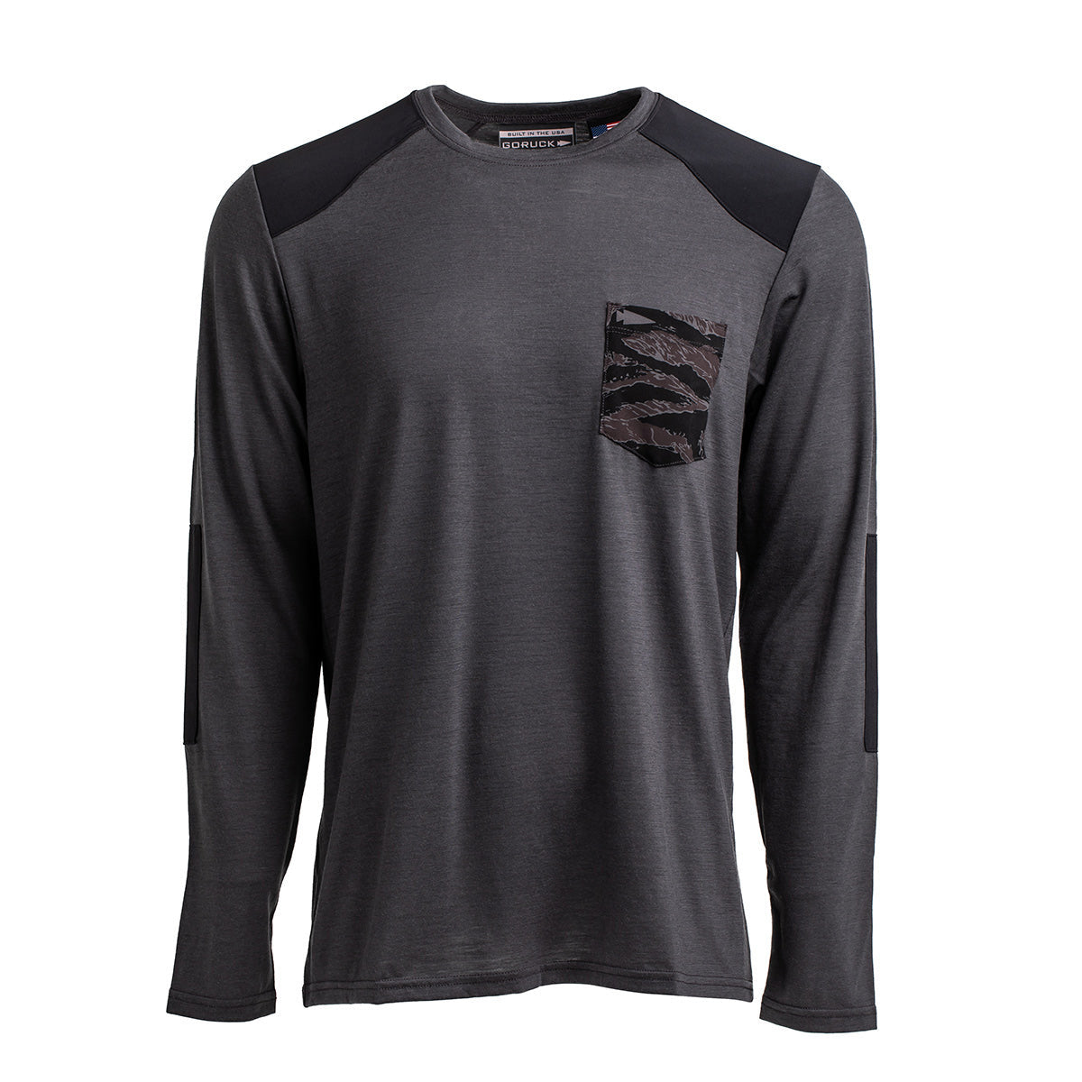 The Men’s Commando Long Sleeve - Merino Wool by GORUCK is a gray, long-sleeved shirt featuring reinforced black shoulder and elbow patches. Made from merino wool, it provides both warmth and style, with a unique chest pocket displaying a black and gray camouflage pattern.