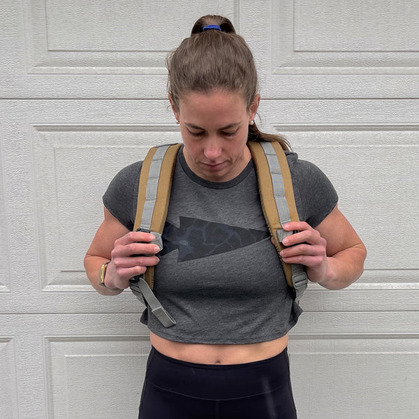 A ponytailed individual, oozing badass babe vibes, is seen rocking a super soft Women's Cropped Tee - Poly-Blend and backpack straps before a garage door.