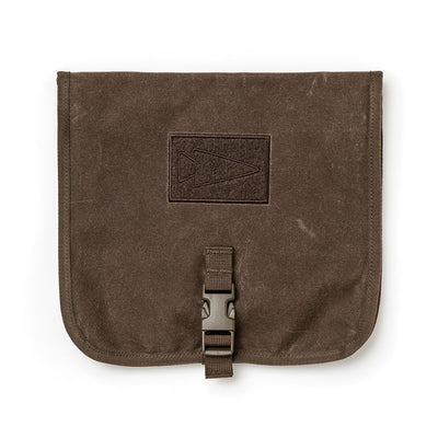 The GORUCK Wire Dopp is crafted from brown waxed canvas, featuring a flap with a buckle closure and an embossed triangle design. The textured fabric emphasizes its durability, making it ideal for organizing travel essentials. Its appearance is both simple and rugged.