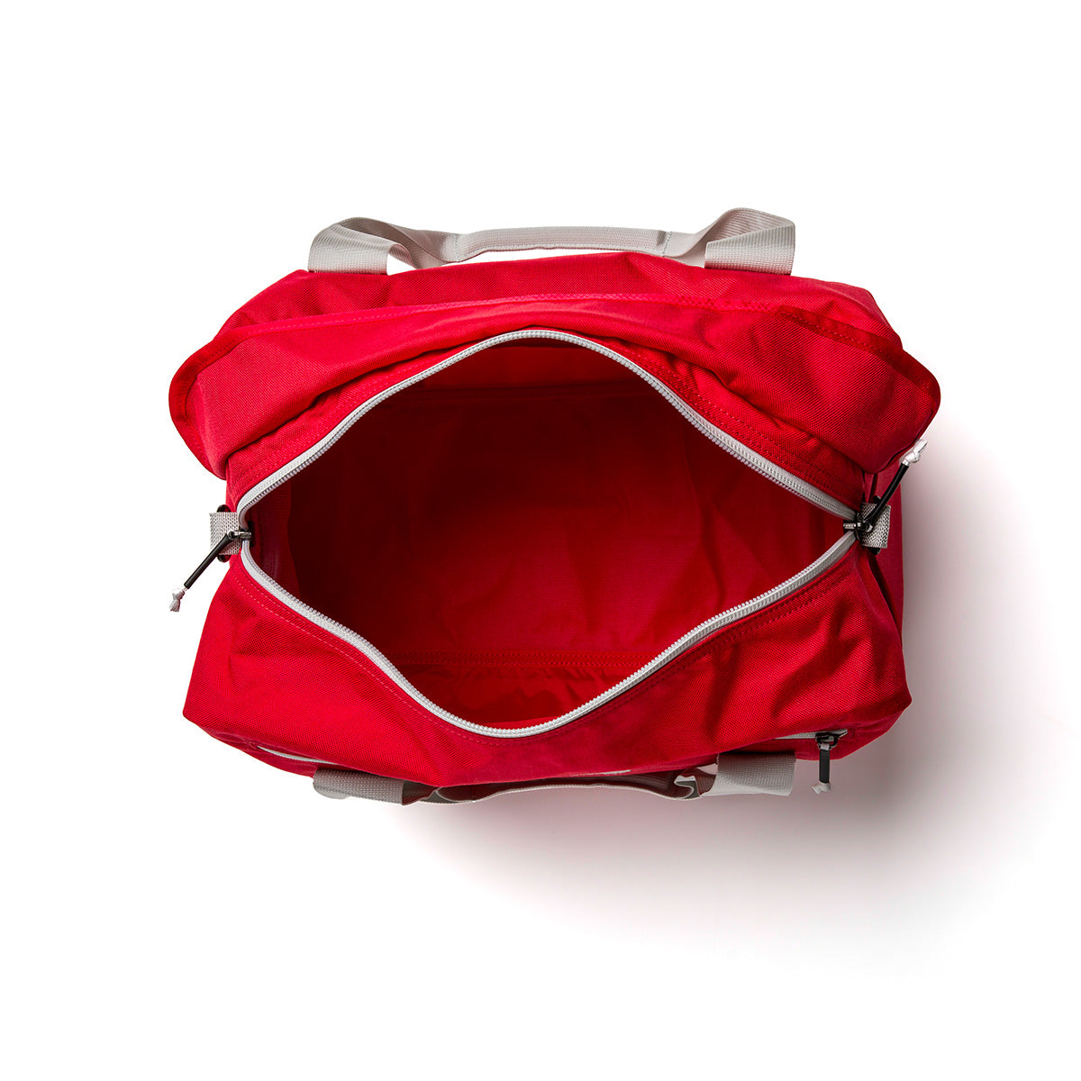 Top view of an open red Kit Bag by GORUCK, featuring a spacious main compartment reminiscent of an Aviator's Kit Bag. The white handles stand out against the plain white background, with the zipper partially open revealing its roomy interior.