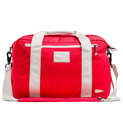 The Kit Bag (Includes Shoulder Strap) is a red duffel with white straps and handles, echoing an aviator's kit bag style, with a small arrow logo on the side.