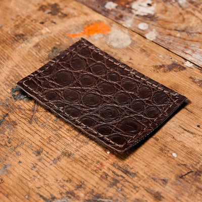 The Everglades Mystery Leather Patches by GORUCK, featuring a crocodile skin texture, rest on a worn wooden surface speckled with paint splatters.