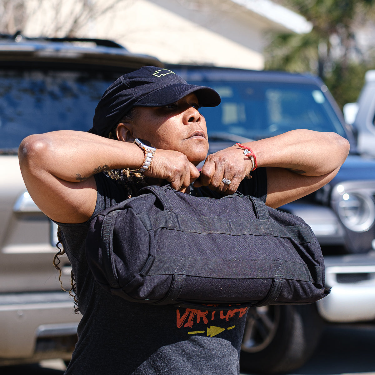 A person lifting a heavy black bag outdoors, sporting a stylish Performance Running Hat - ToughMesh and a t-shirt made from Italian fabric.