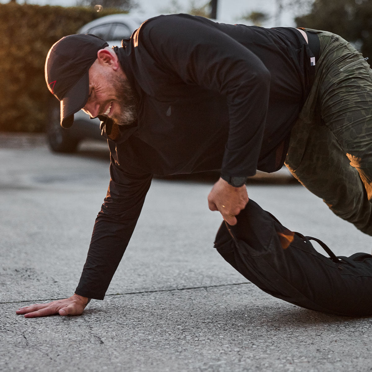 Wearing a black ToughMesh Performance Running Hat made from premium Italian fabric, a person drags a weighted sandbag across the pavement.