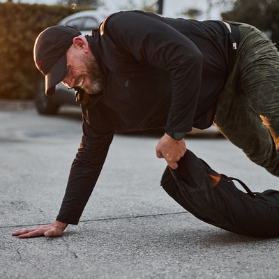 Wearing a black ToughMesh Performance Running Hat made from premium Italian fabric, a person drags a weighted sandbag across the pavement.