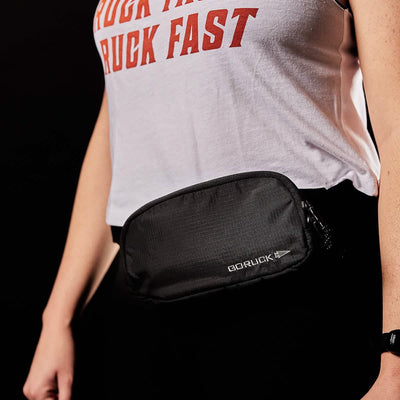 A person in a white tank top with red text sports the GORUCK Belt Bag - Ripstop ROBIC® featuring Waterproof YKK AquaGuard zippers. The dark background adds a touch of mystery.