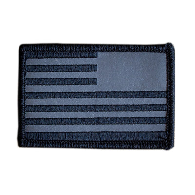 Introducing the Patch - Reflective Reverse Flag by vendor-unknown, a monochrome tactical patch showcasing a stylized U.S. flag with black and gray stripes and stars, meticulously designed as an embroidered patch with VELCRO backing for effortless attachment to uniforms or gear.