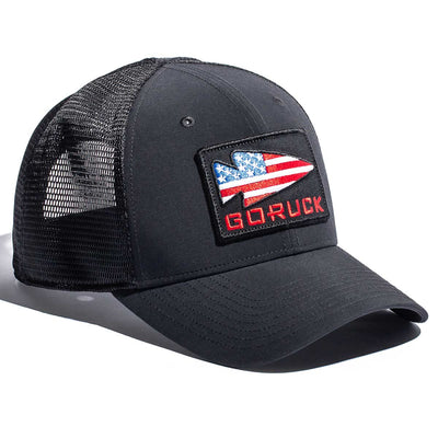 The Performance Trucker Hat - GORUCK USA by GORUCK is a black trucker hat designed with a mesh back. It features a front patch displaying the American flag with the word "GORUCK" in red letters, crafted from sweat-wicking material for added comfort. It also includes an adjustable VELCRO® strap for the perfect fit.